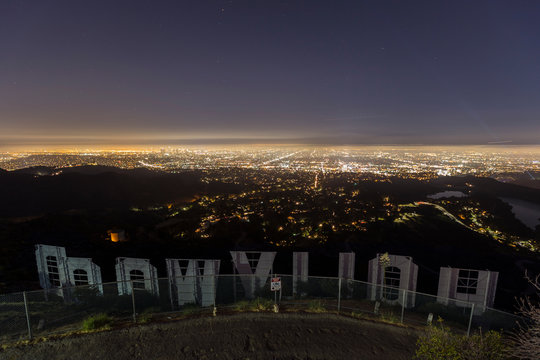 Night view behind the famous Hollywood sign with urban Los Angeles in background on July 2, 2014 in Los Angeles, California, USA.  