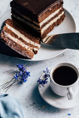 Chocolate cake on a plate and a cup of coffee and lilac flowers for decor on the table close-up
