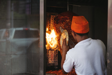 man in front of kebab spits - fire in background