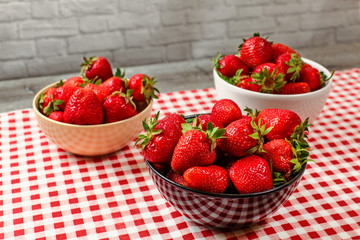 Strawberries in small ceramic bowls on table with red gingham pattern tablecloth