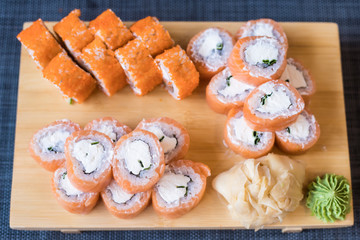 Hand with wooden chopsticks takes rolls that stand on a wooden stand and blue litter, blurred background, close up. Flat lane