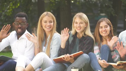 Group of young students sitting together on green lawn high school university campus.