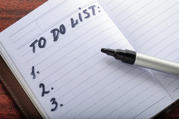 To do list written in personal notepad with empty space and black marker on dark desk. Planning and design concept.