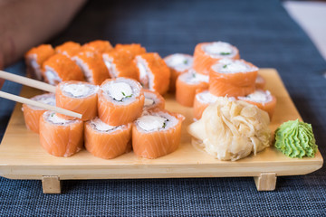 Hand with wooden chopsticks takes rolls that stand on a wooden stand and blue litter, blurred background, close up.