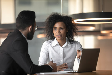 Mixed race businesswoman and colleague discussing project, using laptop