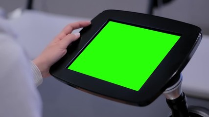 Close up view: woman using floor standing tablet kiosk with blank green display at exhibition, training classroom, museum. Education, green screen, mock up, copyspace, template, chroma key concept