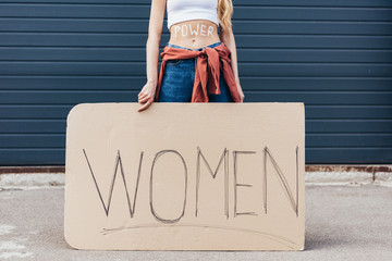 cropped view of feminist with inscription power on belly holding placard with slogan women on street