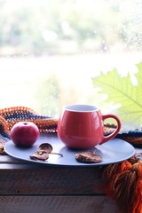 Bright cup with coffee on a window background, apples on a plate, warm scarf, leaves, autumn season, home comfort concept