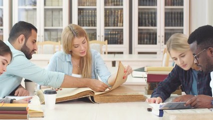 Diverse multiracial students spending leisure time in library with big old book.