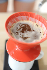 Brewing coffee drip method. Pouring water from gooseneck kettle into red hario v60 funnel.