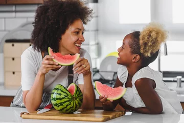 Fotobehang Beautiful African Mother and Daughter eating Watermelon at Home Kitchen © lordn
