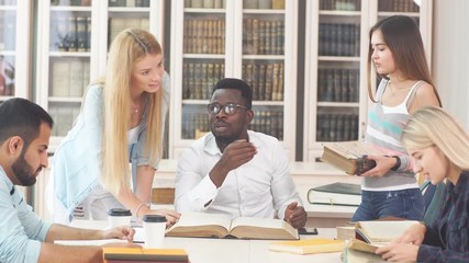 Group of young students doing school assignment in library.