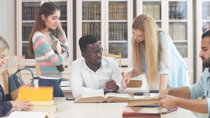 Diverse multiracial students spending leisure time in library with big old book.