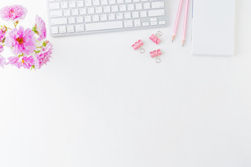 Flat lay blogger or freelancer workspace with a notebook, keyboard and pink flowers on a white...