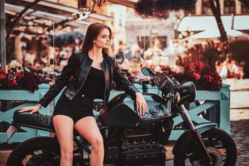 Naklejka na ściany i meble Beautiful sexy woman in mini shorts is posing on the motorbike at busy city centre.