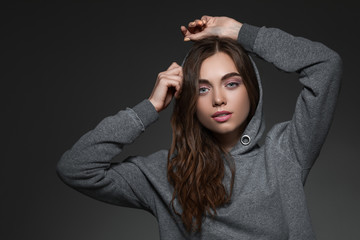 portrait of beautiful woman with long hair in hood on gray background. girl looking at camera.