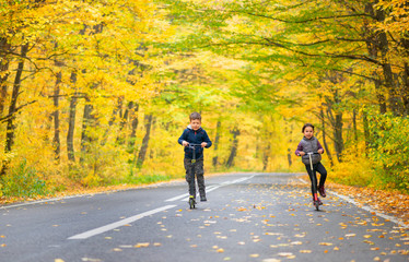 two kids with scooter on the autumn street