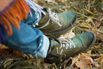 Close-up of a leg in green hiking boots with laces in the autumn forest against a background of yellow fallen foliage, selective focus