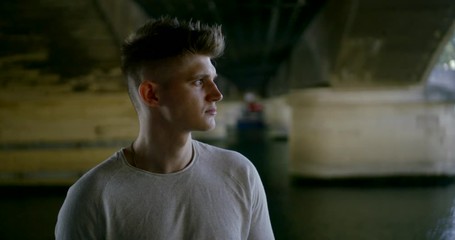Close-up portrait of a young man standing under a bridge near the river Seine, posing.