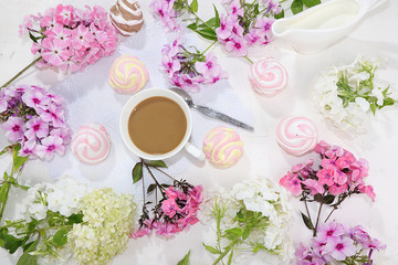 Colorful flowers of pink phlox, a cup of coffee and marshmallows on a light table, top view, flat lay, selective focus. Pink flowers on a light background, a gift for loved ones,