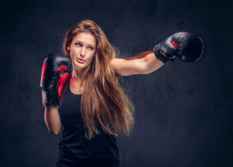 Beautiful woman with long hair is demonstraiting her hit at studio. She is wearing boxing gloves.