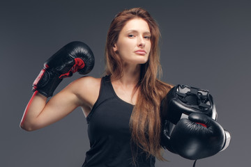Beautiful woman wearing boxer gloves is holding protective helmet while posing for photographer.