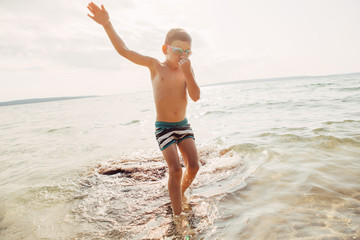 Cute funny Caucasian boy swimming in lake river with underwater goggles. Child diving in water on beach. Authentic real lifestyle happy childhood. Summer fun outdoor aquatic activity.