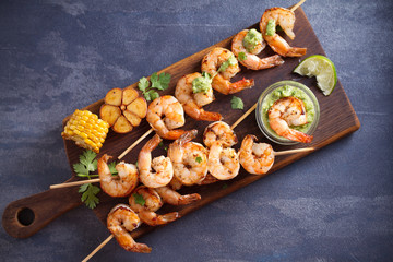 Obraz na płótnie Canvas Skewered shrimps with garlic butter sauce served with cilantro and lime on serving board