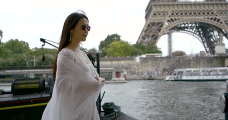 Asian middle-aged woman who walks in Paris on the background of the Eiffel tower and the river Seine. She has dark glasses on her face and the wind is blowing her hair