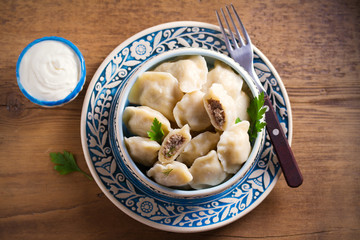 Pierogi or pyrohy, varenyky, vareniki - dumplings in bowl served with sour cream or yogurt on wooden table