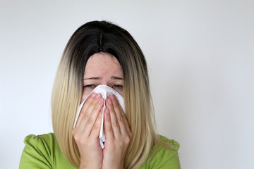 Sick woman sneezing and blowing her nose in a handkerchief. Concept of colds and flu, runny nose,...