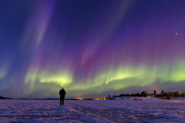 Personne regardant un spectacle à couper le souffle d& 39 aurores boréales colorées sur le lac gelé Inari, en Finlande.