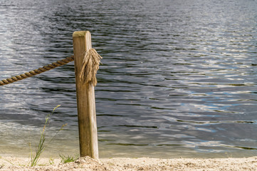 A wooden pole with a rope on sand beach with water background.