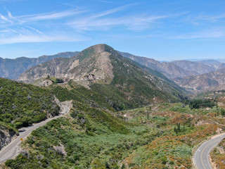 Fototapeta premium Asphalt road bends through Angeles National forests mountain, California, USA. Thin road winds between a ridge of hills and mountains at high altitude