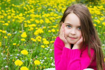Fototapeta premium Cute little girl is sitting in a field with dandelions.
