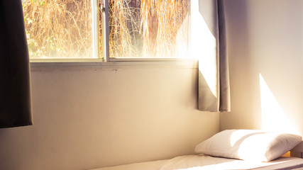 cheap motel room interior with bed and white sheet near window with morning sun rise soft yellow light 