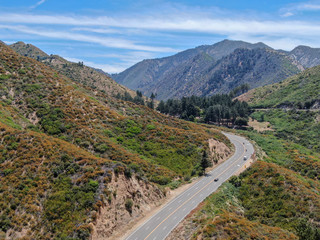 Fototapeta premium Asphalt road bends through Angeles National forests mountain, California, USA. Thin road winds between a ridge of hills and mountains at high altitude