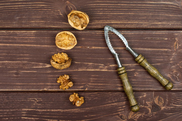 Group of three whole two pieces of ripe brown walnut with old nutcracker flatlay on brown wood