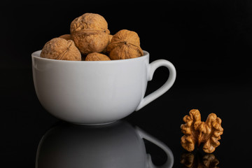 Lot of whole ripe brown walnut one is aside without shell and the rest is in white ceramic cup isolated on black glass