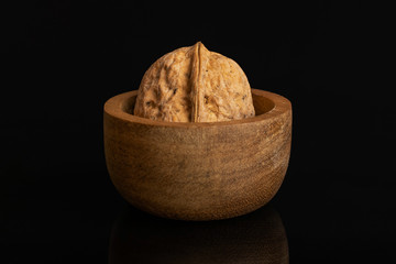 One whole ripe brown walnut in tiny wooden bowl isolated on black glass