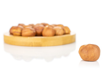 Lot of whole ripe brown hazelnut one is in front and rest is in back on round bamboo coaster isolated on white background