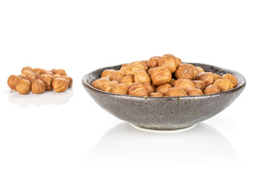 Lot of whole ripe brown hazelnut part is aside and part is in dark ceramic bowl isolated on white...