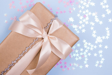 Beautiful gift box with beige bow and pink glitter stars on a pastel blue background. Flat lay.