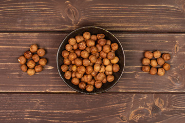 Lot of whole ripe brown hazelnut in dark ceramic bowl flatlay on brown wood