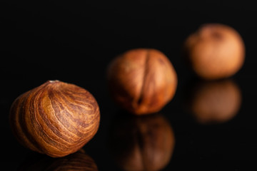 Group of three whole ripe brown hazelnut placed diagonally in line in closeup isolated on black glass