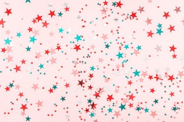 Multi-colored stars glitter on pink background. Festive holiday pastel backdrop. Celebration concept. Decorative Christmas and New Year party background. Top view, flat lay. Horizontal