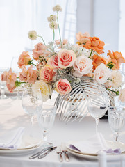 Table served for wedding banquet with cutlery and flowers in vases. Pastel colored decorations.