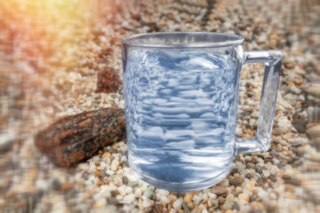 A glass of water stands on the sand.