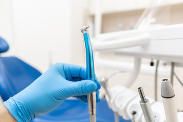 Close-up hand of dentist in the glove holds dental high speed turbine. Office where dentist conducts inspection and concludes.