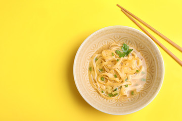 Cooked noodles with herbs and chopsticks on yellow background, flat lay. Space for text
